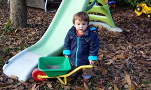 Kleiner Junge mit Kinderschubkarre vor einer Rutsche - Herbststimmung