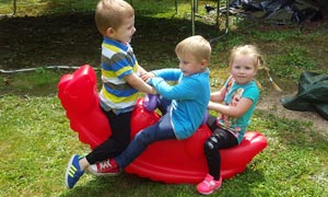 Drei Kinder im Garten auf einer roten Wippe.